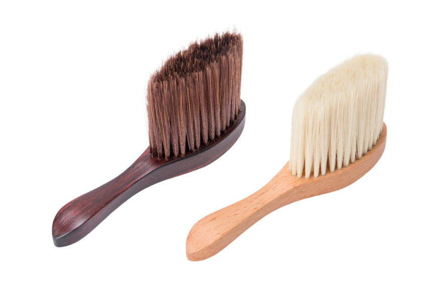 Two brushes, one with brown bristles and wooden handle, the other with white bristles and wooden handle, on a light background.